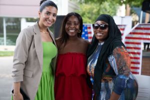 Three women smiling together at outdoor event.
