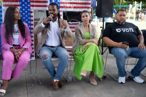 Panelists seated in a row discuss topics at an outdoor event decorated with American flags.
