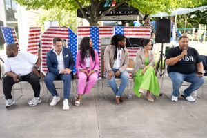 Diverse panel members seated in chairs at an outdoor event with American flag decorations.