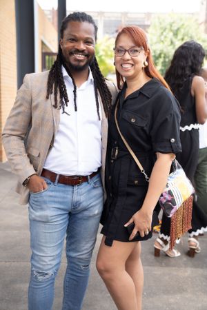 Two friends pose together at a social gathering wearing casual smart attire.