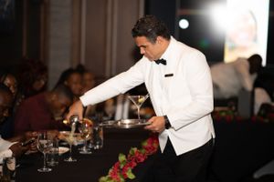 Server in white jacket pouring drinks at elegant event with floral table decorations.
