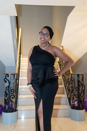 Person in elegant black evening dress poses on ornate staircase with decorative railings.