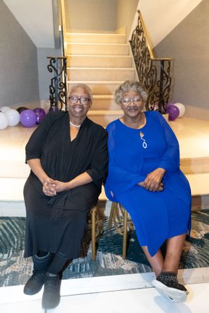 Two people in formal attire seated on stairs with purple balloons and decorative railings.