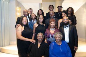 Group photo of formally dressed people arranged on elegant stairs.