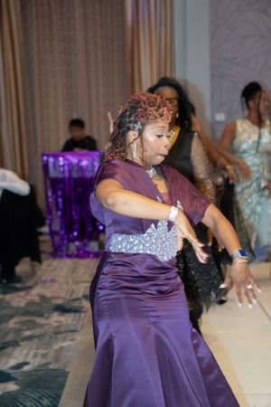 Guest in purple gown dances energetically at formal event.