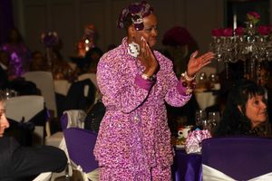 An entertainer in a shimmering purple outfit performs at a formal dinner event with decorated tables.