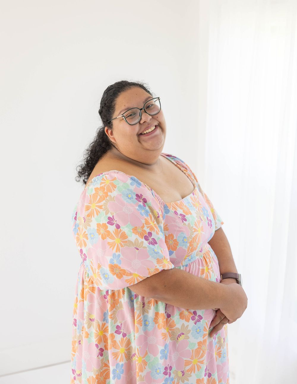 Woman in floral pink dress posing joyfully against white background.