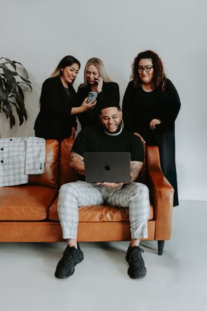 A group of people gathered around a laptop on an orange couch share a light moment in a modern office setting.