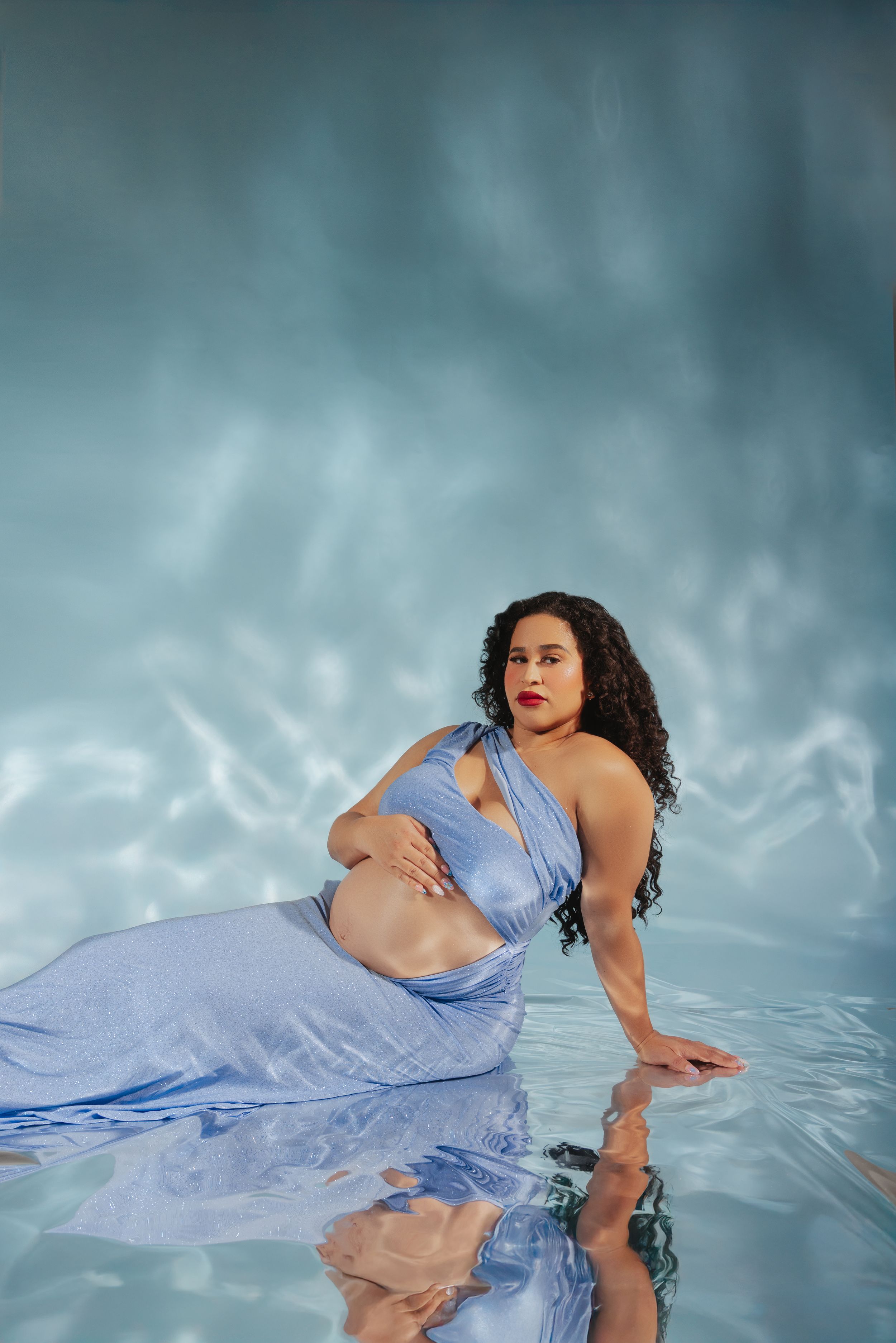 Ethereal portrait of someone in a flowing periwinkle dress reclining gracefully in dreamy blue-tinted water.