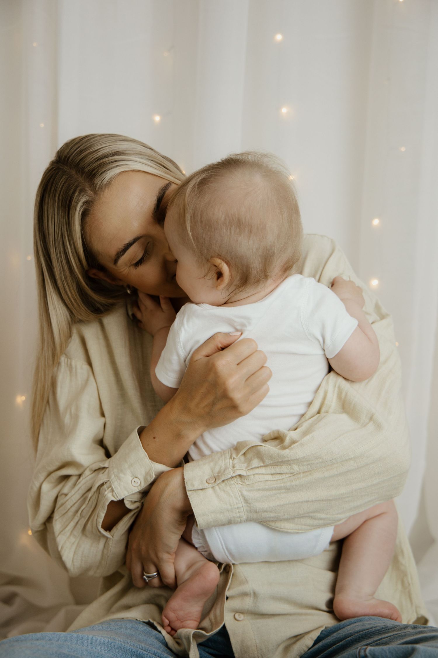 Woman with black nail polish and charm bracelet wearing leopard print cardigan holding a baby's hand.