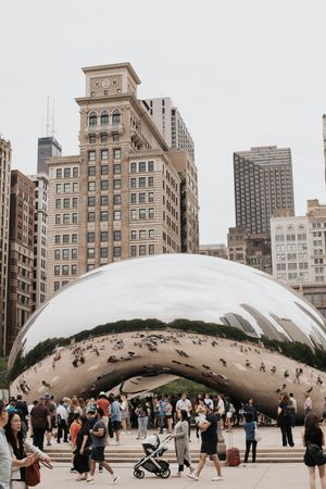 The Chicago bean on a cloudy day with people walking by.