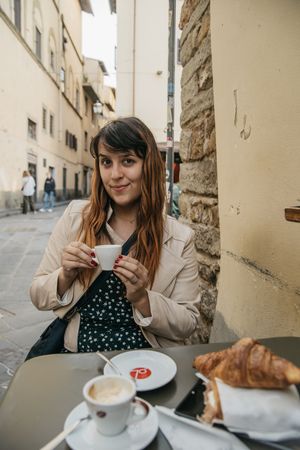 Photographer Kelsey Nevell sits at a table in Florence Italy holding an espresso.
