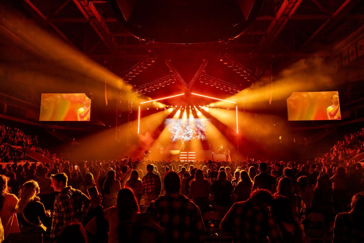 Concert venue with dramatic lighting and silhouetted crowd during a live performance.