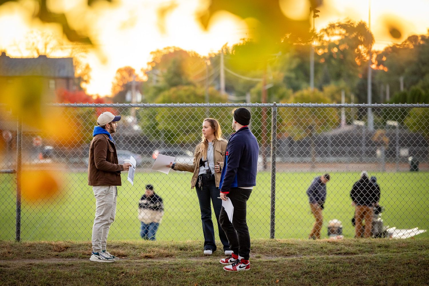 People gathered on a sports field at sunset with golden bokeh lighting effects.