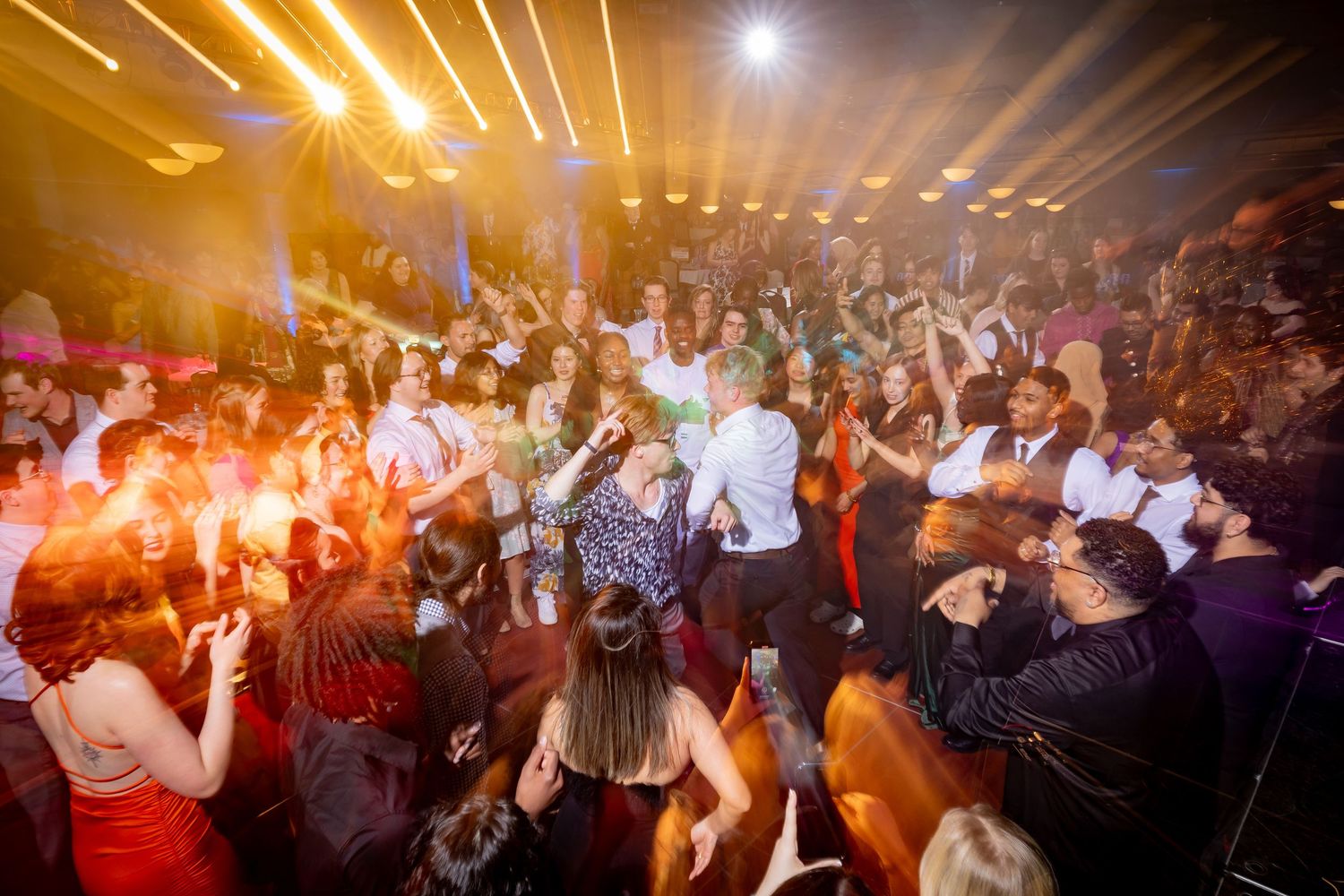 Crowded dance floor illuminated with warm lighting and special effects at an event.