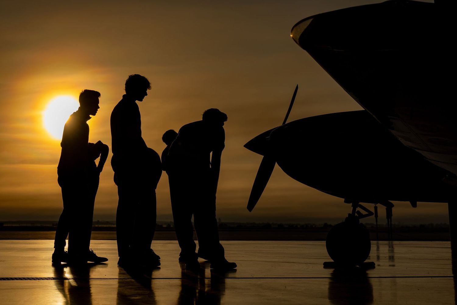 Silhouettes of people against a dramatic sunset sky near an aircraft.