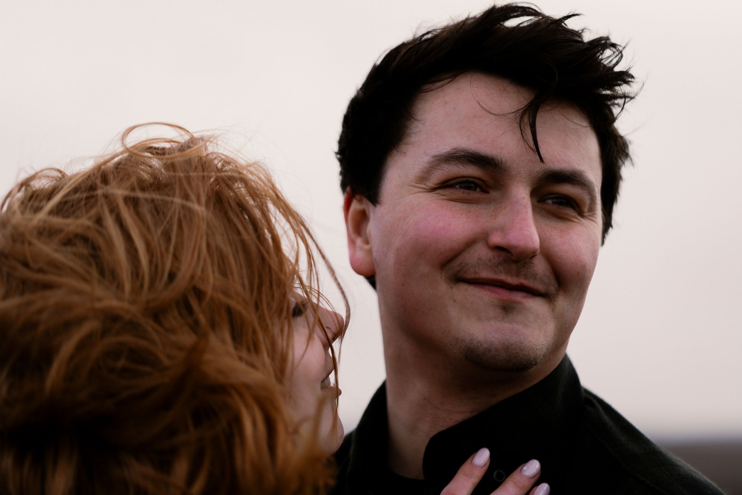 A candid, natural moment of a couple — joyful, relaxed expressions and wind-tousled hair capture raw emotion and genuine connection.