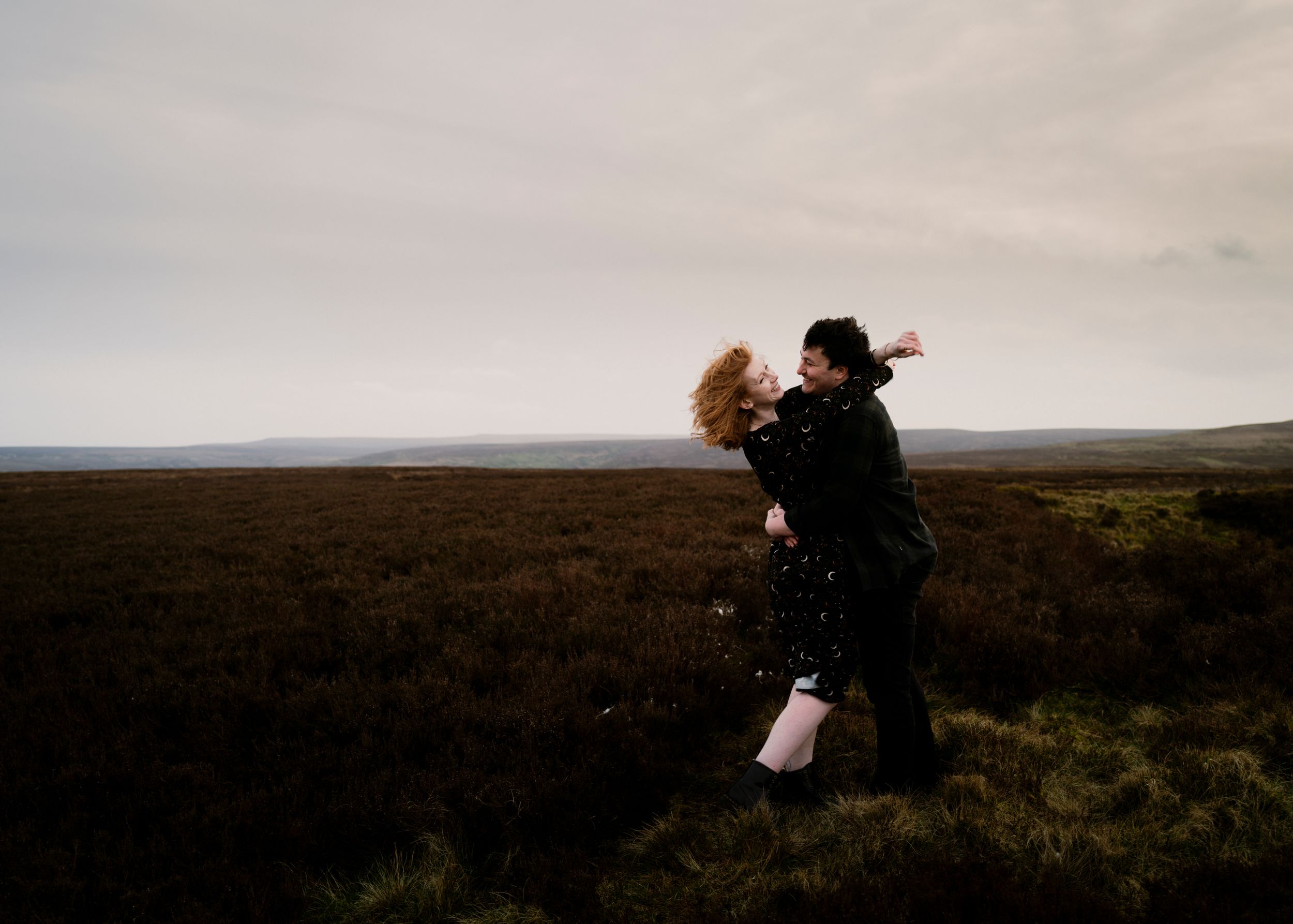 A candid, natural moment of pure joy — a couple laughing and embracing in an open field, capturing their love in its most genuine form.
