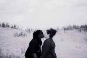 A tender moment captured in the dunes — a soft, blurred kiss, timeless and intimate. LGBTQ+
