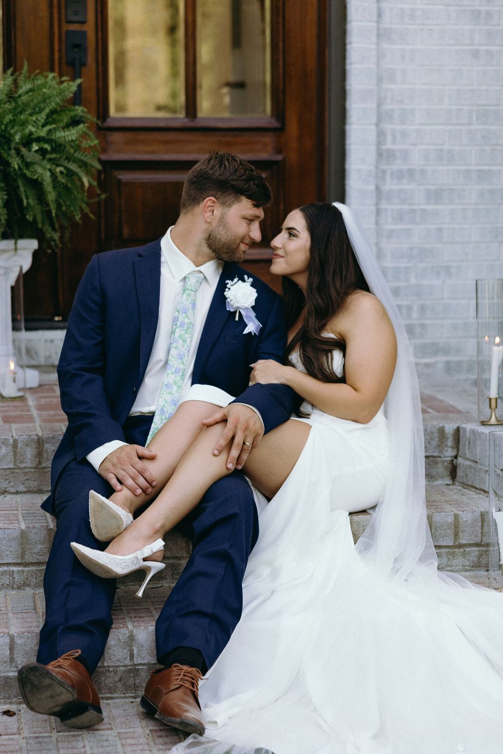 Wedding couple shares intimate moments while seated on stone steps of white building. The Bradford, Separk  Mansion, Graylyn Estate