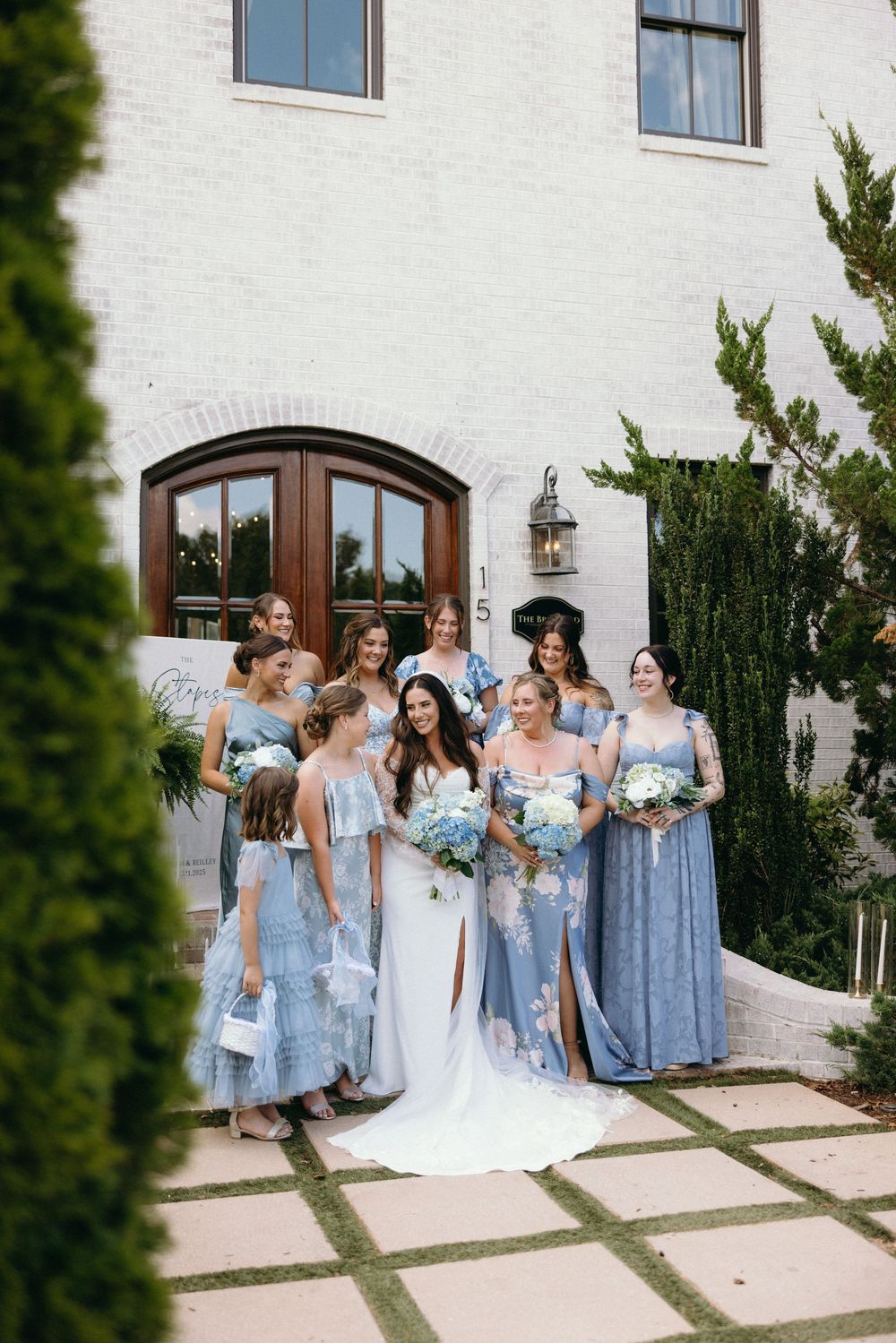 Wedding party in light blue bridesmaid dresses poses together outside a white building. The Bradford, Separk  Mansion, Graylyn Estate