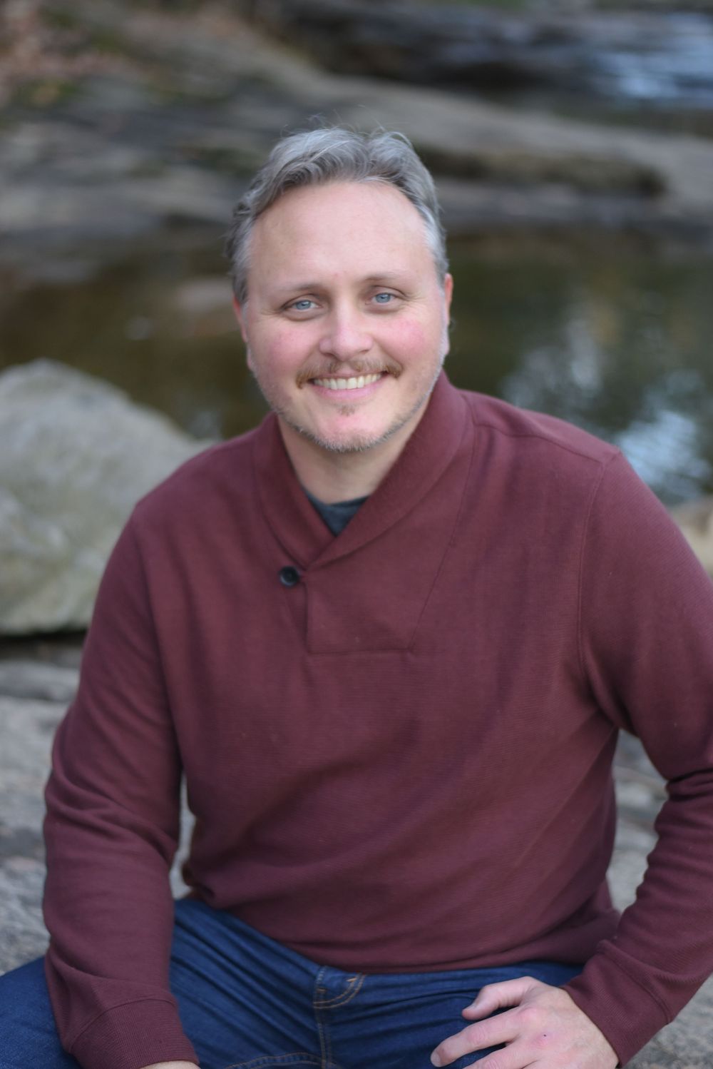 Casual portrait of person wearing burgundy sweater sitting outdoors.