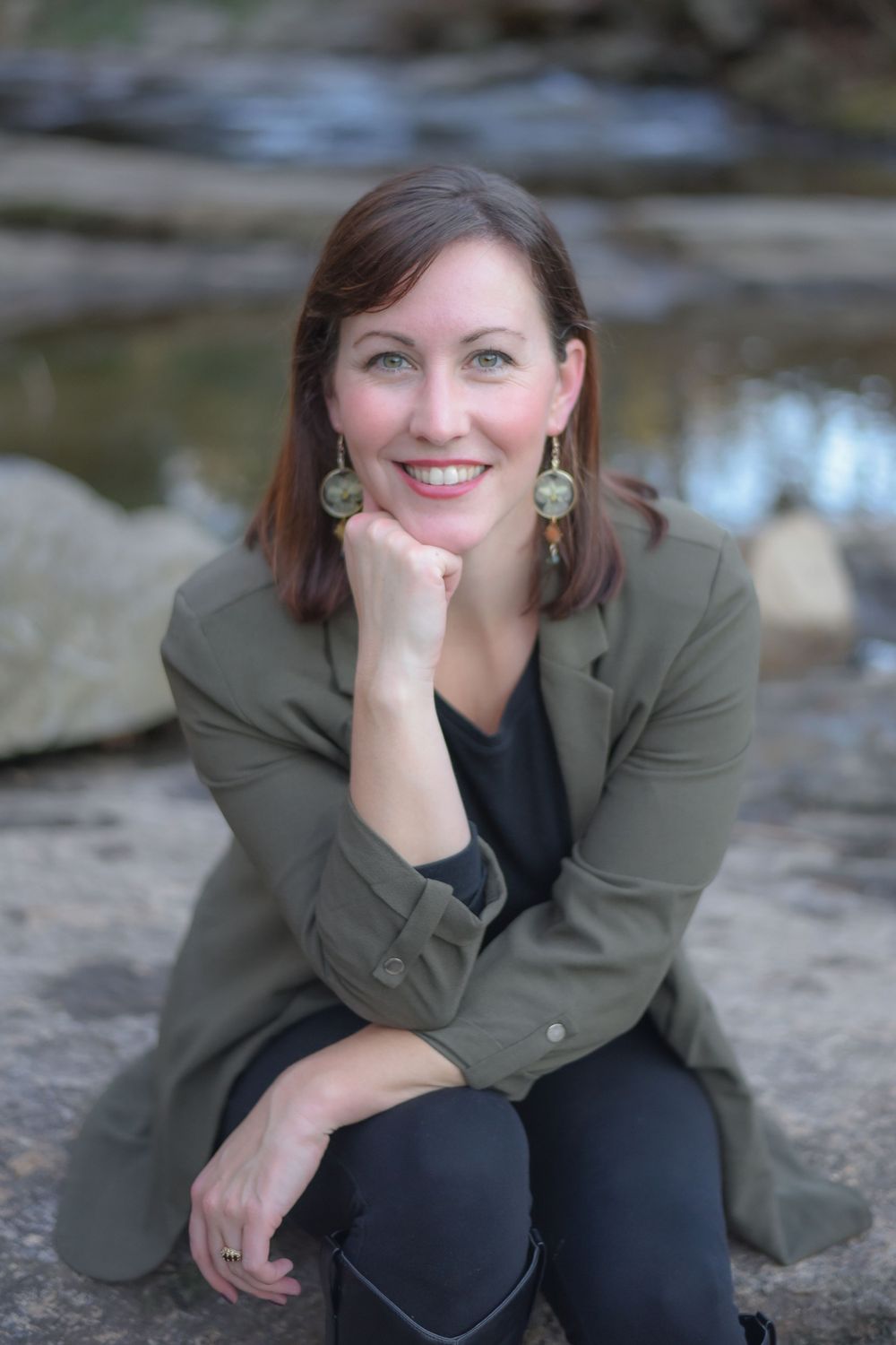 Casual outdoor portrait session on rocky riverbank with person in green blazer.