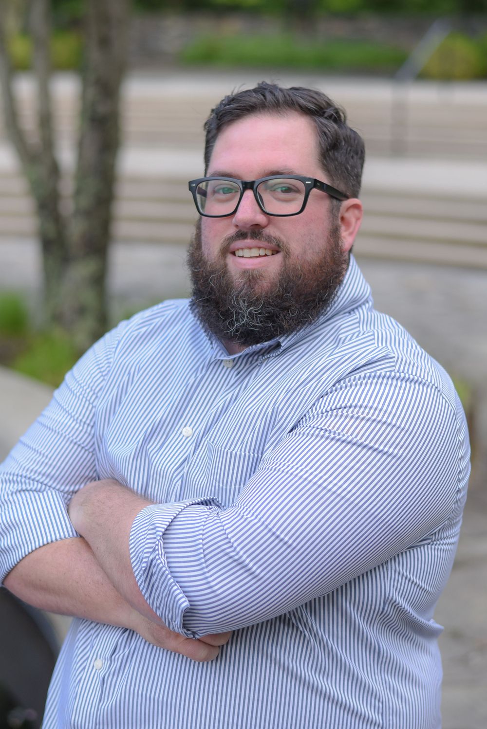 Professional portrait of person in striped shirt and glasses with crossed arms.