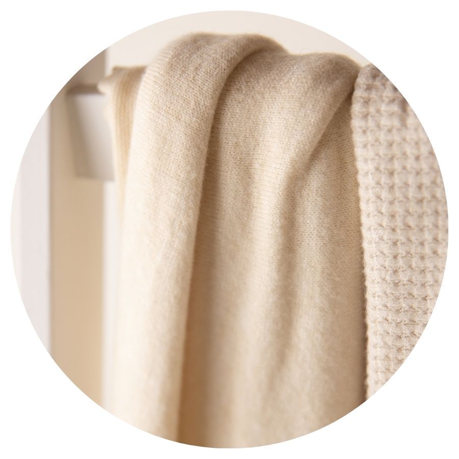 Soft cream cashmere throw blanket draped elegantly over a rack, showcasing its luxurious texture and neutral tone.