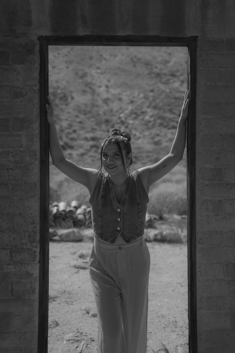 Artistic black and white photo of person framed in doorway with arms raised against desert backdrop.