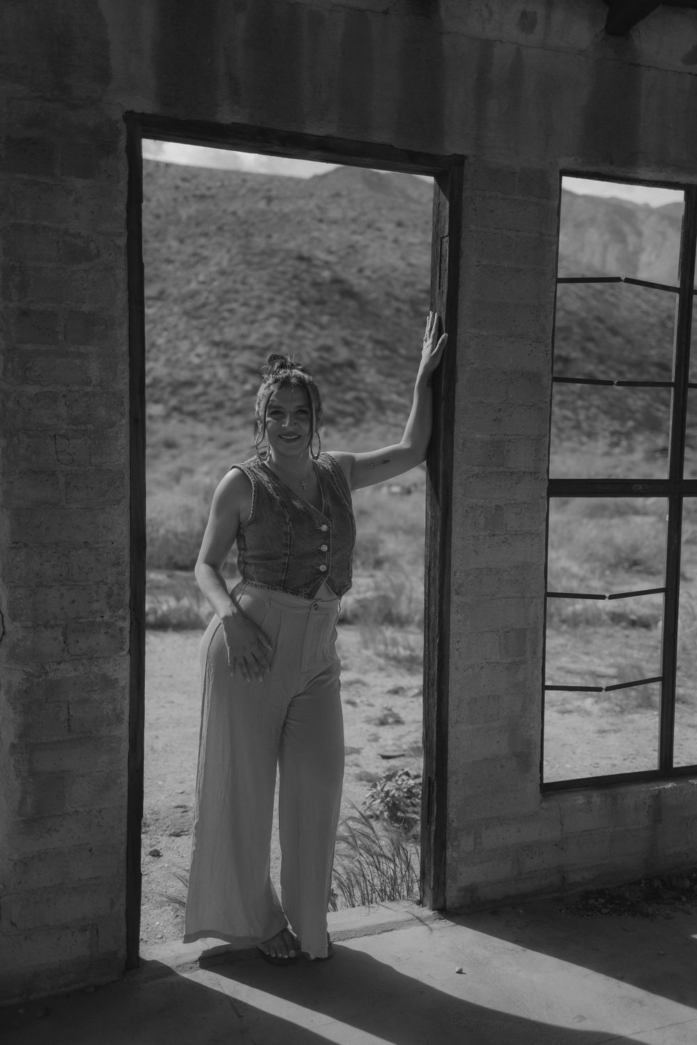 Black and white image of person standing in sunlit doorway of abandoned desert building.