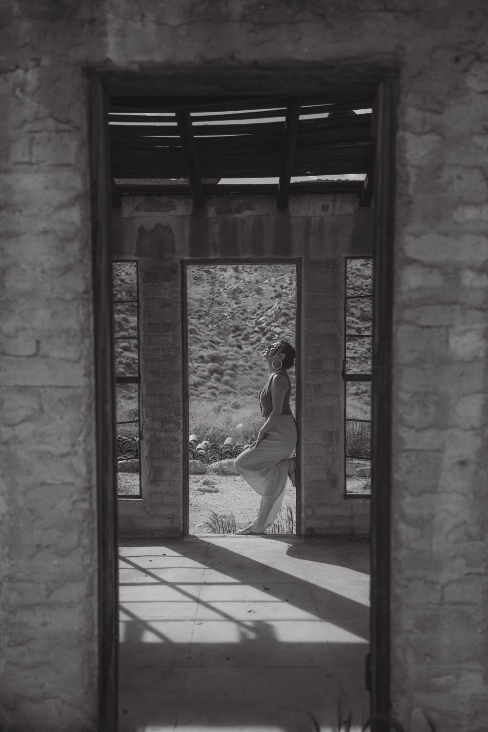Dramatic black and white photo showing figure through doorway with geometric shadows.