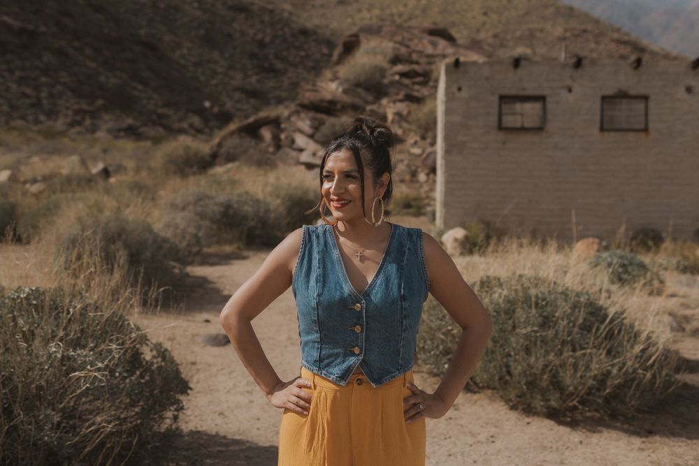 Someone in denim and yellow pants poses confidently outside a desert building.