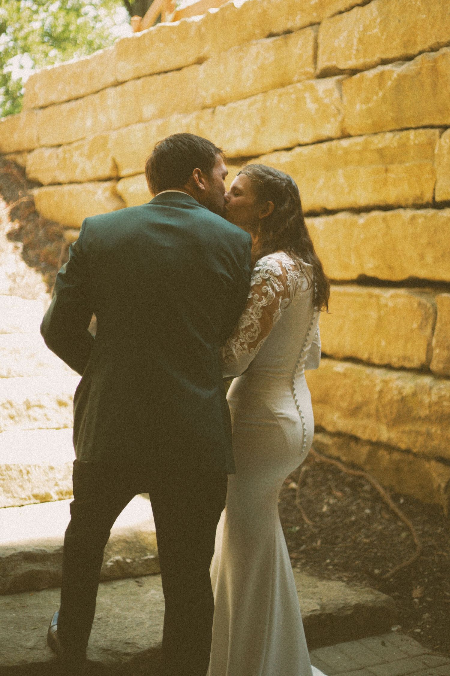 Couple shares intimate moment against golden stone wall in wedding attire.