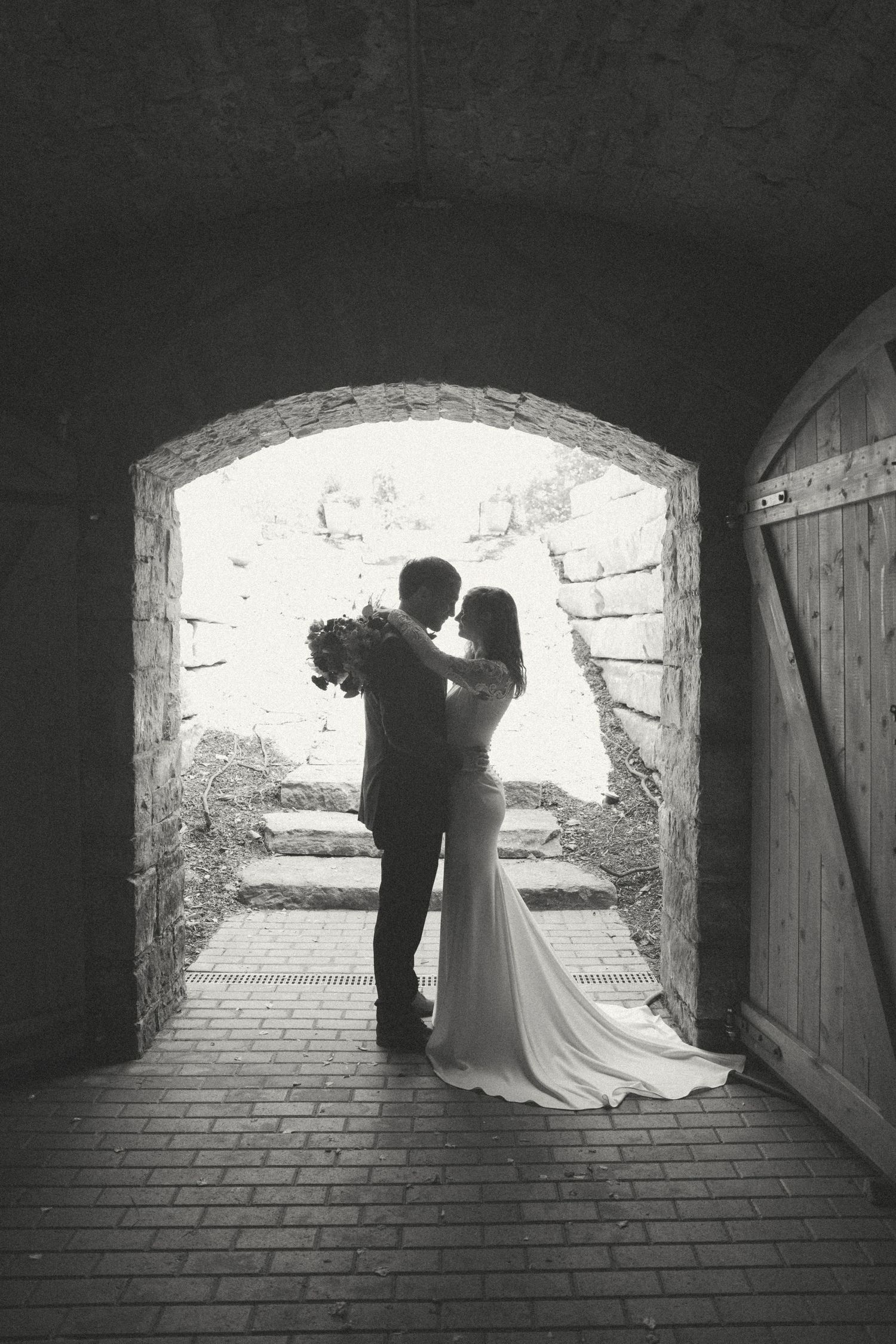 Silhouetted couple embraces in stone archway creating dramatic wedding portrait.