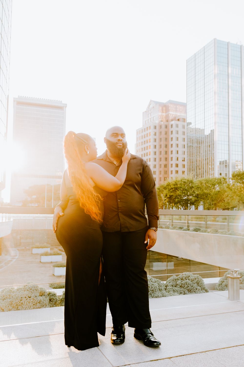 A couple embraces in front of modern city buildings during golden hour.