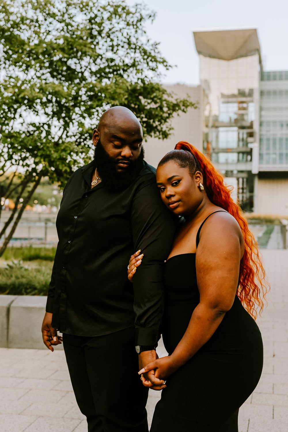 A stylish couple in black outfits poses together in an urban setting.