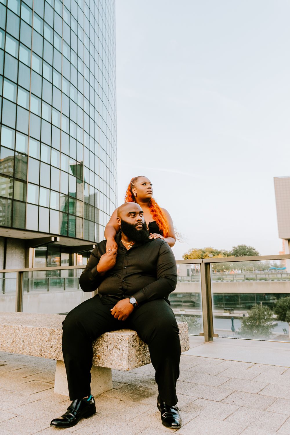 An urban couple poses dramatically against a modern glass building in the city.