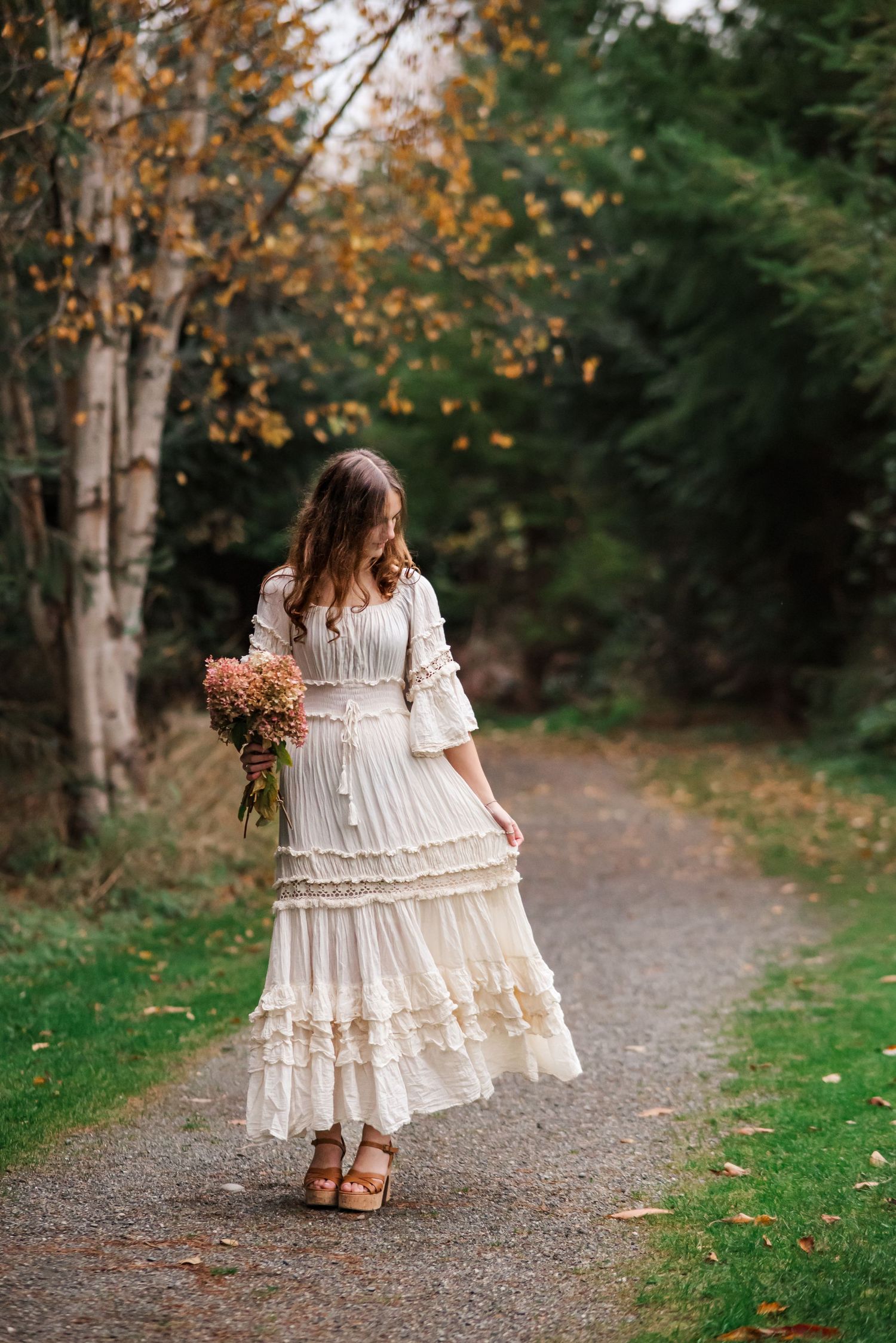 senior girl swishes dress in fall holding a fall bouquet of hydrangeas from her garden