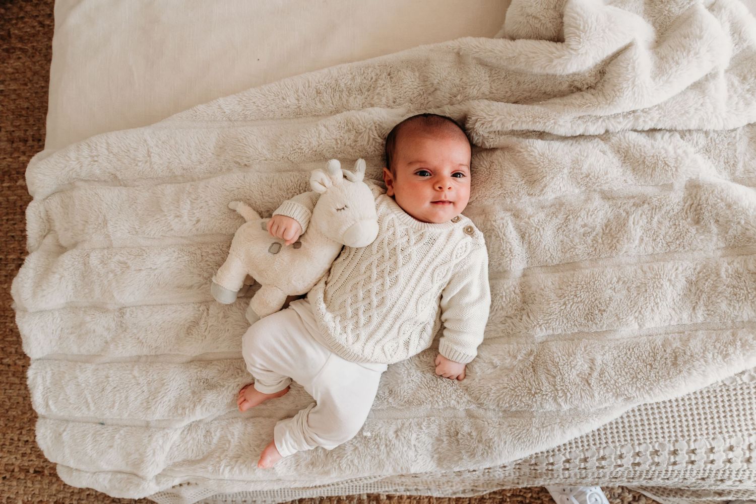 Baby in white sweater lying on plush blanket with stuffed animal during their Connecticut in studio photography session.