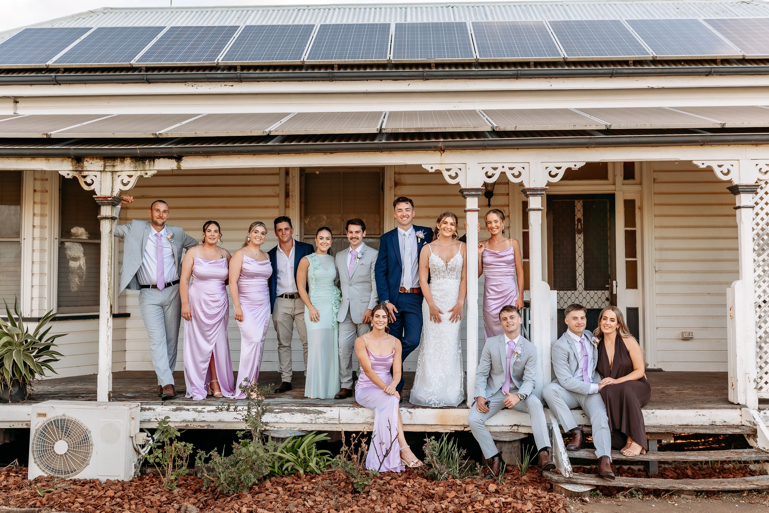 Wedding party gathers on the wraparound porch of a classic white house.