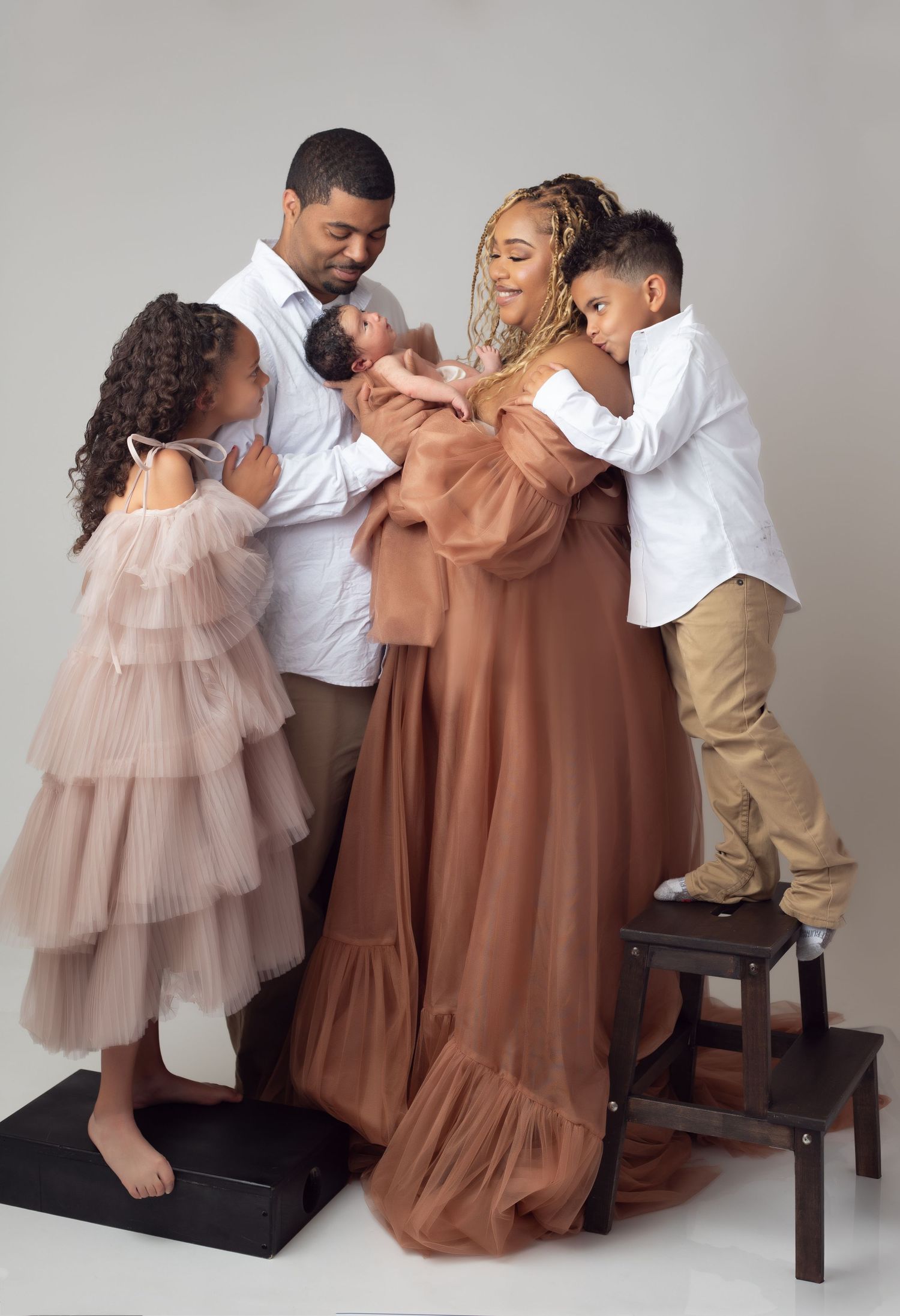 Intimate family photoshoot with newborn, two other children, Mom and Dad, against white background.