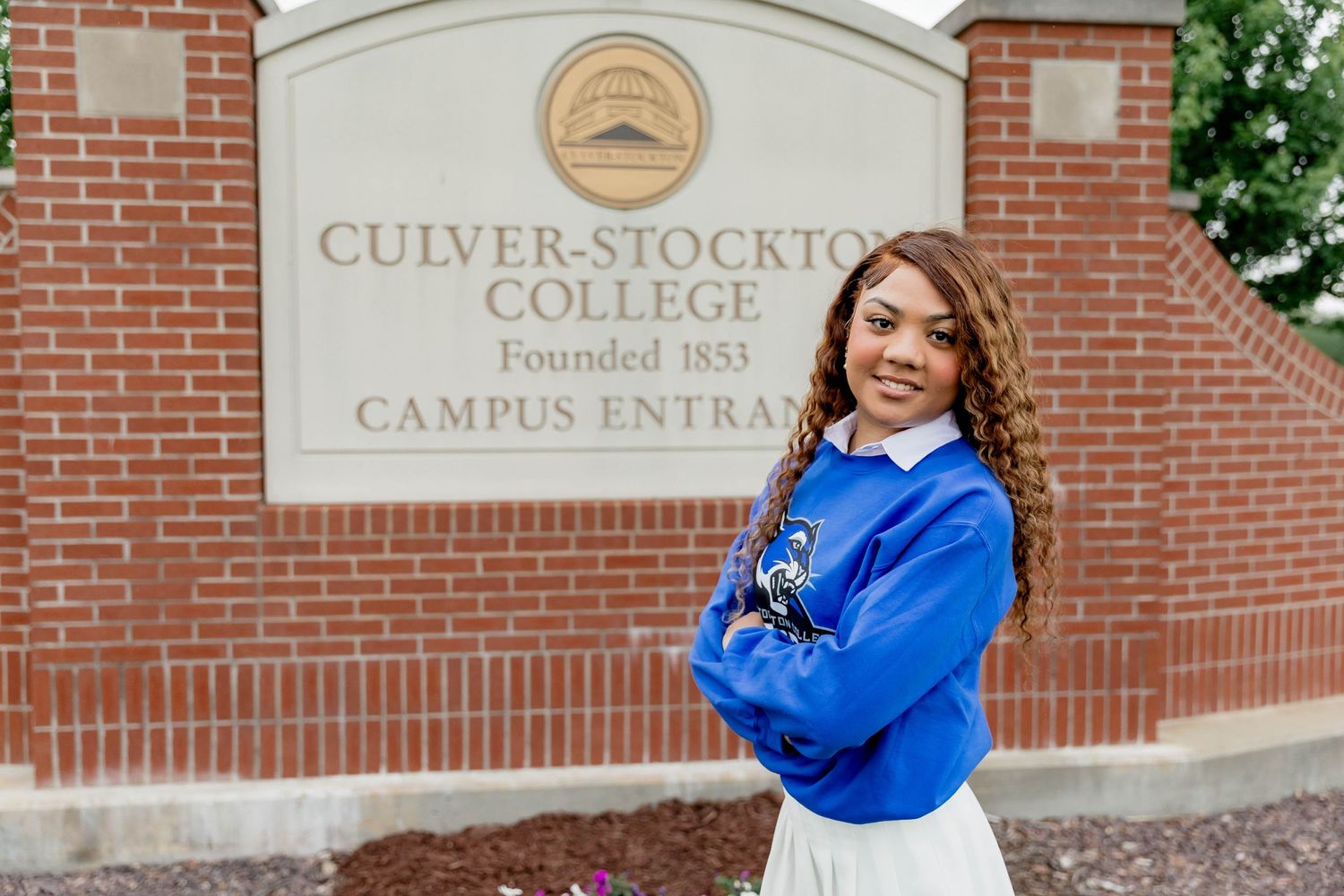 Student poses in front of Culver-Stockton College brick entrance sign wearing bright blue.