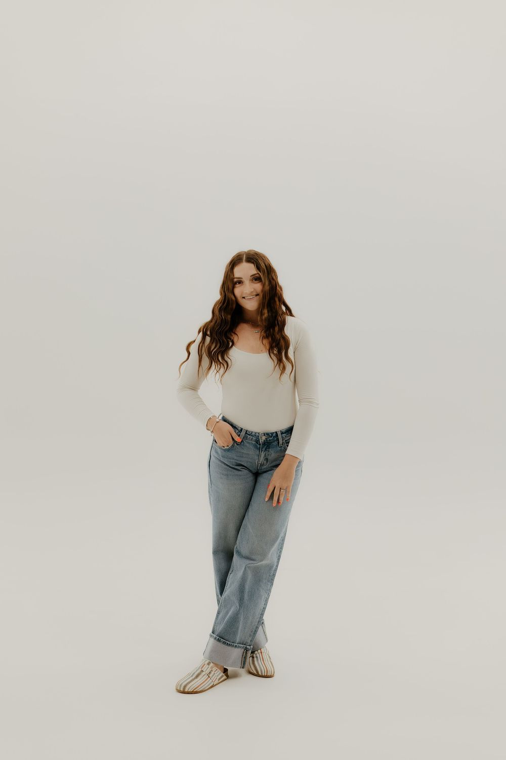 Model in blue jeans and white sweater poses casually against white backdrop.