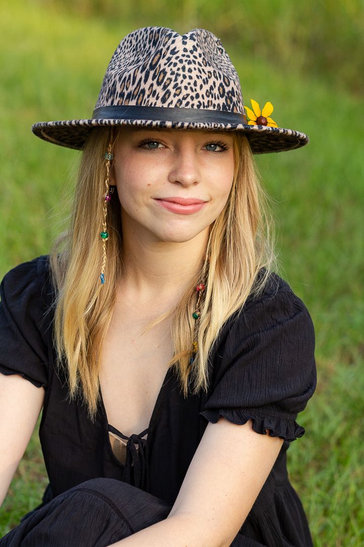 Portrait in nature wearing a leopard print hat with a yellow flower and black dress.