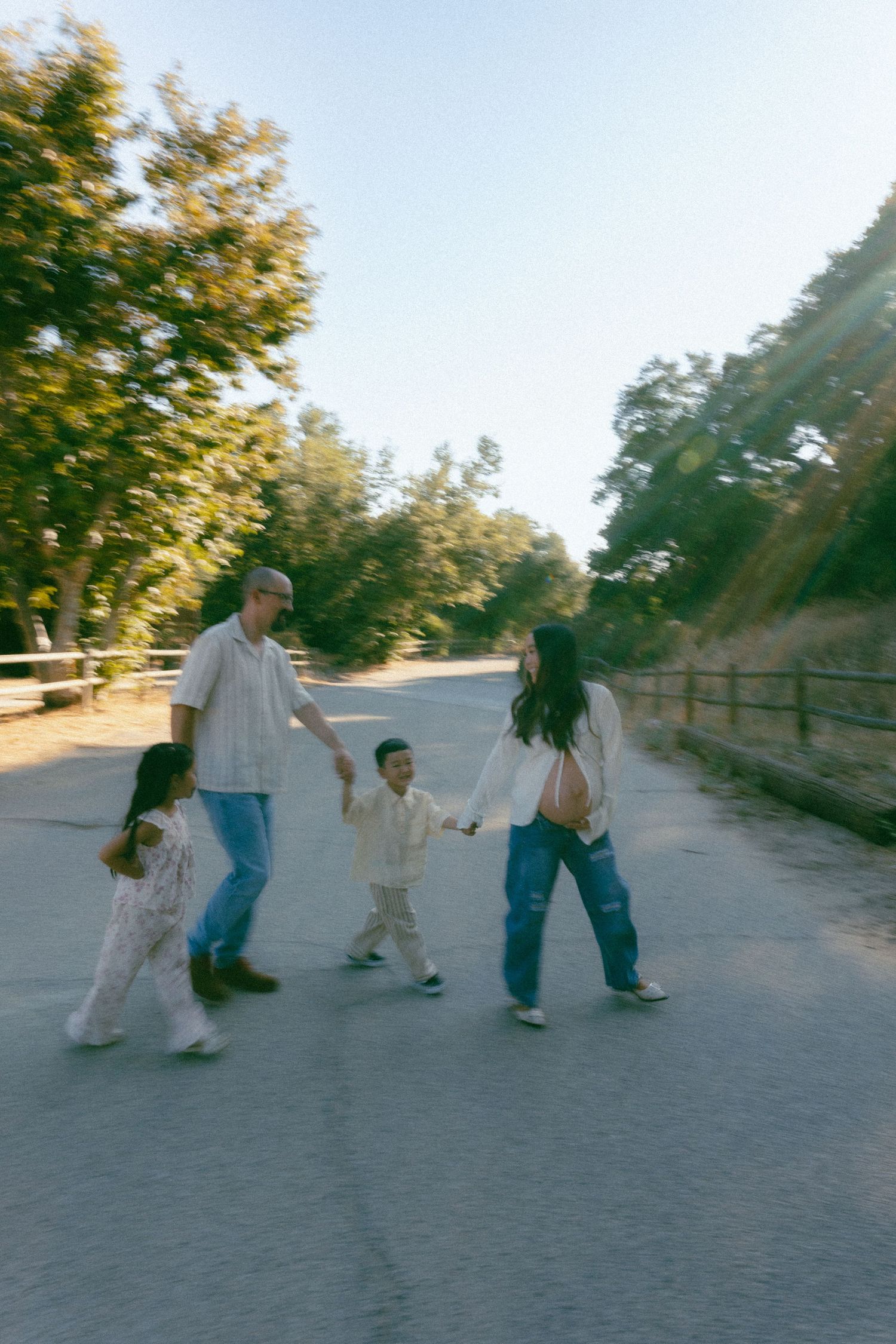 Four figures walking together on a sunlit path with trees visible in the background.