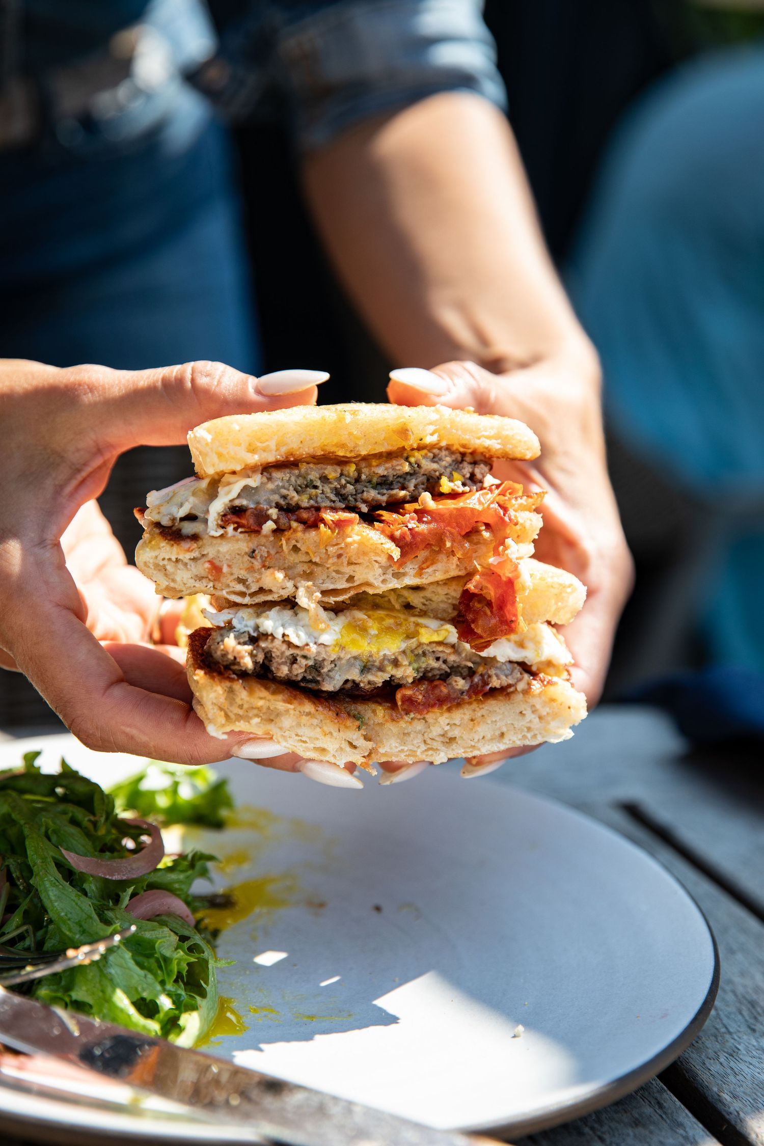 Juicy double cheeseburger with melted cheese and toppings held over a plate with side salad.