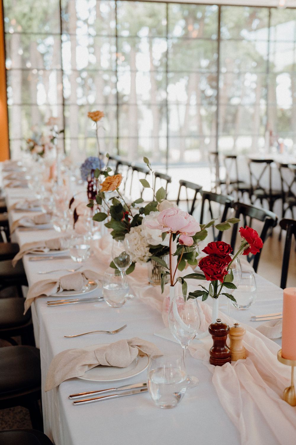 Formal table setting with colorful floral arrangements and place settings in bright venue.