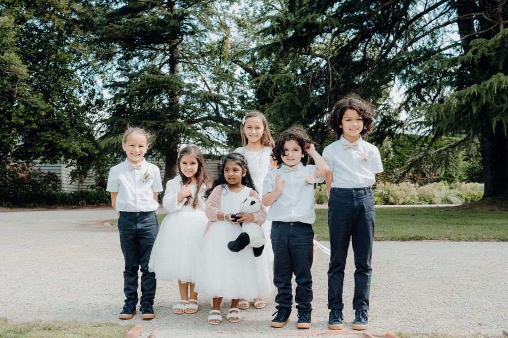 Children in formal white and blue attire pose together outdoors.
