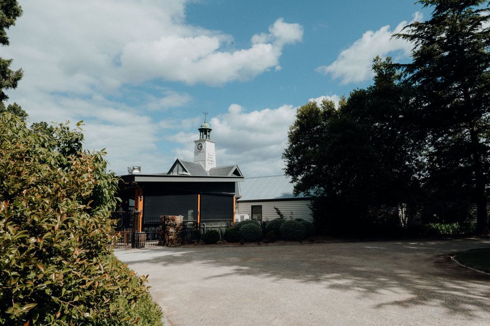 White building with black roof and chimney surrounded by trees on sunny day.